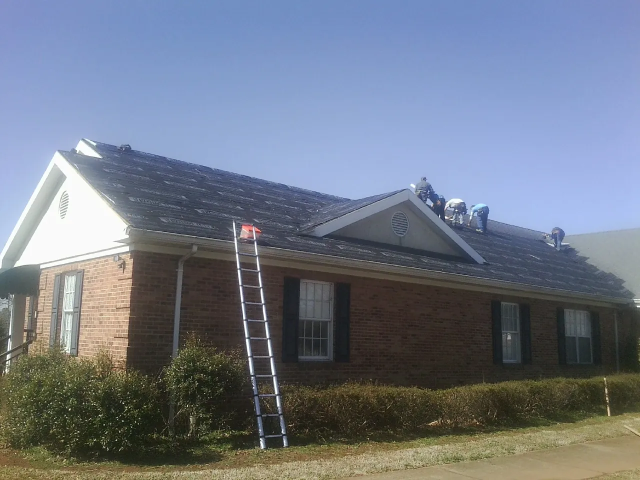 Crew tearing shingles off a brick ranch roof with a ladder set — Metal Roof Repair work by our crew in Dorchester Center