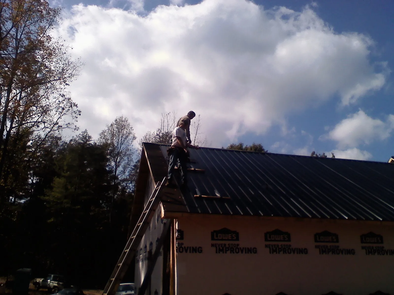 Roofer fastening dark metal panels high against a cloudy sky, from a Roof Inspection job in Dorchester Center