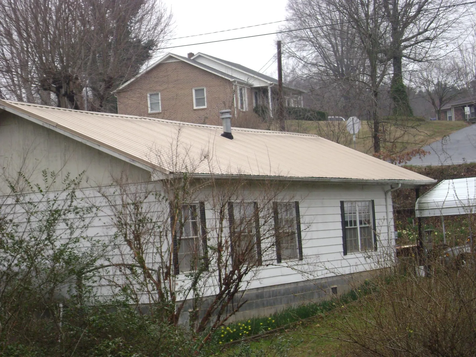 Tan metal roof on a white sided house set into a hillside — Commercial Roofing by Roofing Brothers in Dorchester Center